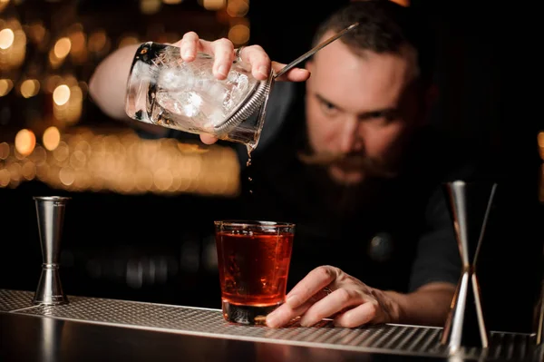 Cantinero con barba vertiendo cóctel de alcohol usando vidrio con colador — Foto de Stock