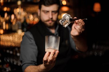 Maşalarla cam ve buz tutan barmen portresi
