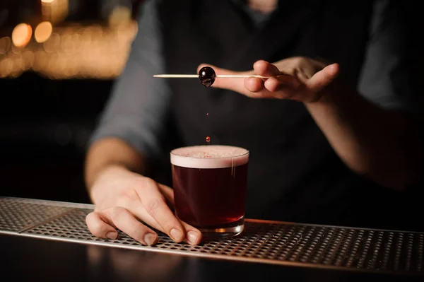 Bartender decorating alcohol cocktail with cherry on toothpick — Stock Photo, Image