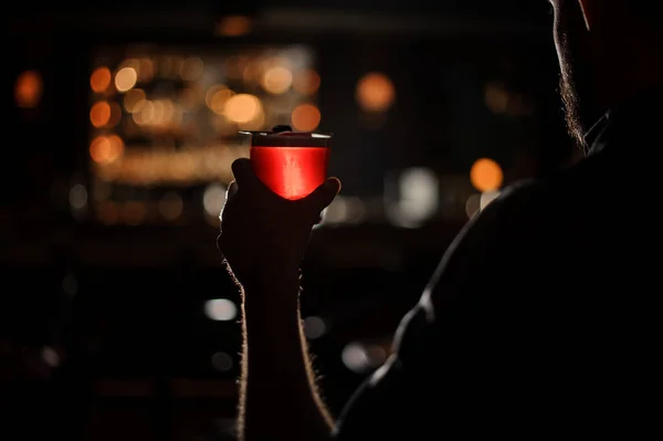 Darkened shot of bartender with red alcohol cocktail