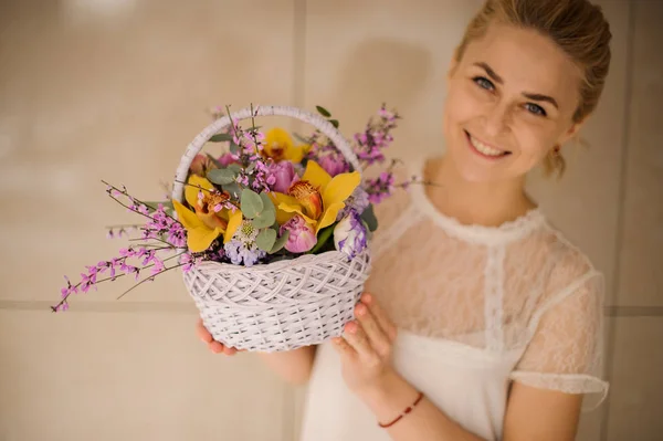 Frau lächelt und hält kleinen Korb mit Blumen — Stockfoto