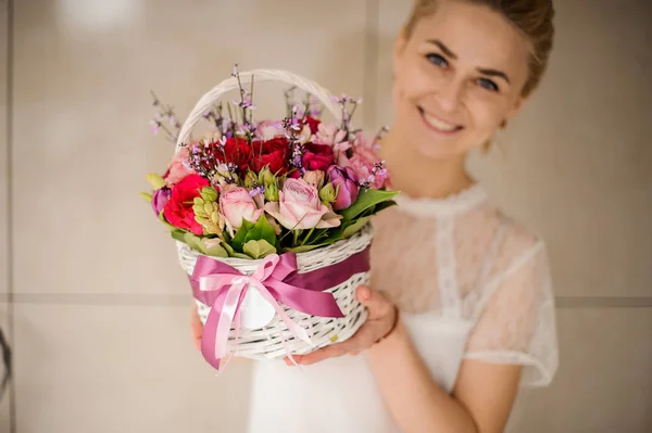 Menina jovem sorri e segura pequena cesta com flores — Fotografia de Stock