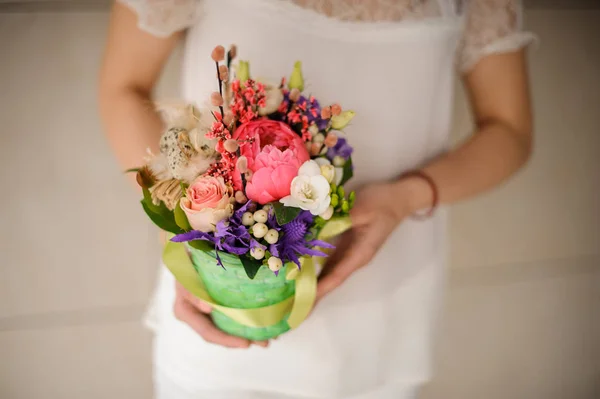 Woman in white dress holding a spring green pot of tender pink, white and violet flowers — 스톡 사진