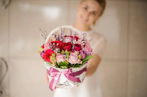 Menina sorridente segurando uma cesta branca primavera de rosas vermelhas e rosa — Fotografia de Stock