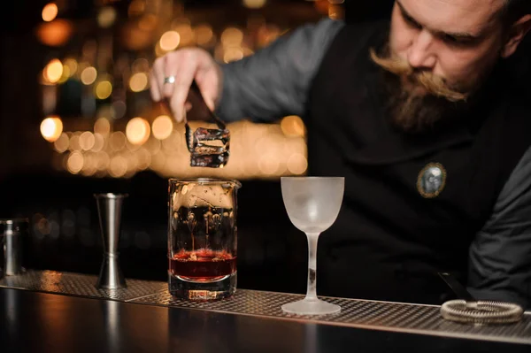 Cantinero poniendo un cubo de hielo a la taza de vidrio medidor — Foto de Stock