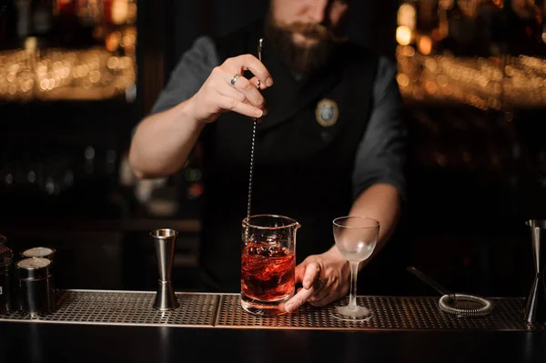 Barman revolviendo un cóctel rojo con una cuchara de acero en la taza de vidrio medidor —  Fotos de Stock