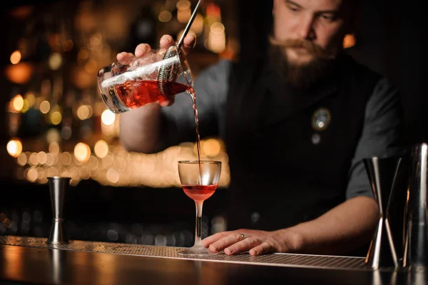 Бармен наливает красный коктейль из чашки с мерным стеклом — стоковое фото