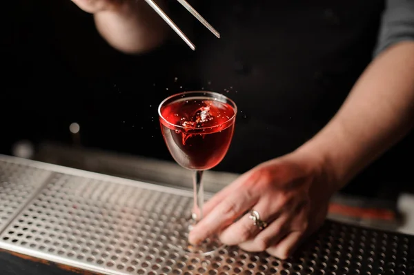 Barman adicionando uma decoração de uma baga vermelha com pinças para o coquetel — Fotografia de Stock