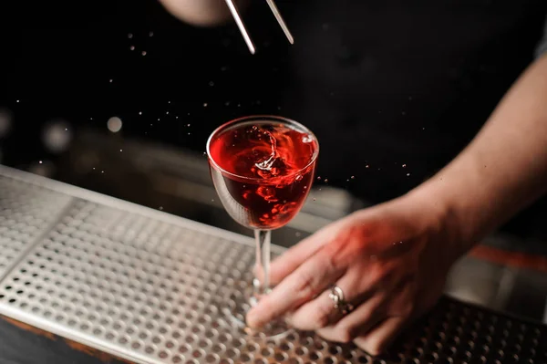 Male bartender adding a decor of one red berry with tweezers to the cocktail