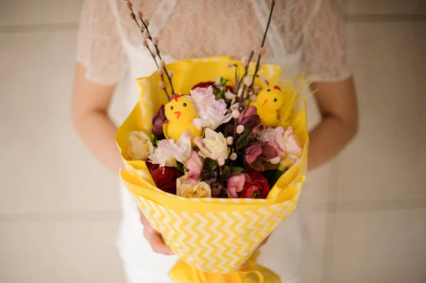 Menina segurando um buquê de primavera de flores rosa e escuras em papel amarelo — Fotografia de Stock