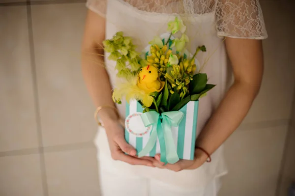 Mulher segurando uma pequena caixa de primavera de flores verdes decoradas com frango de brinquedo — Fotografia de Stock