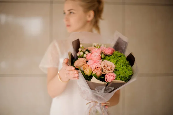 Attrayant femme tenant un bouquet de tendres fleurs printanières crémeuses et vertes de couleur rose — Photo