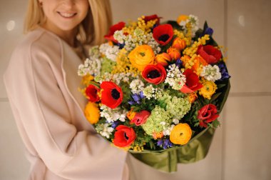 Çok renkli çiçeklerden oluşan bir bahar buketi tutan gülümseyen kız