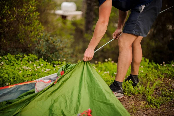 Young man sets up a green tent putting in a metal frame
