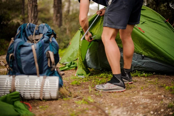 Un jeune homme installe une tente verte dans un cadre métallique près du matériel de randonnée — Photo