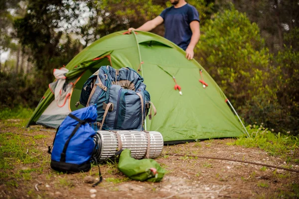Homem monta uma tenda verde perto do equipamento de caminhada — Fotografia de Stock