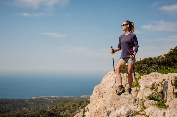 Aantrekkelijk meisje staande op de rots in shorts met wandelstokken — Stockfoto