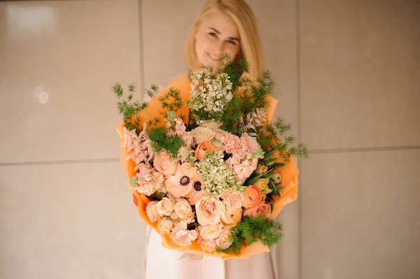 Smiling girl in the coat holding a bouquet of tender peach color flowers — Stock Photo, Image