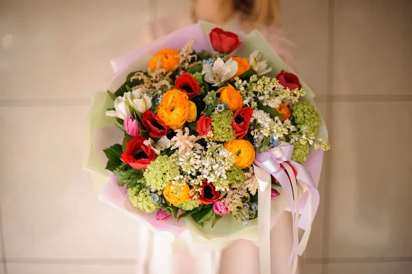 Girl in the coat holding a bouquet of tender red, orange and green flowers — Stock Photo, Image