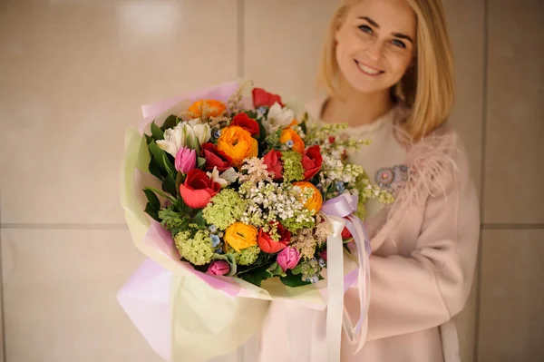 Gülümseyen kız ihale kırmızı, turuncu ve yeşil çiçek bir buket tutan