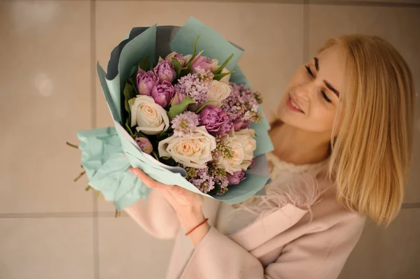 Mujer sonriente mirando el ramo de tiernas flores de color violeta brillante y melocotón — Foto de Stock