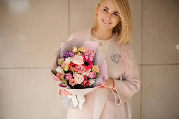 ผู้หญิงที่ยิ้มในเสื้อโค้ทถือช่อดอกไม้สีอ่อน ดอกไม้หลากสีชมพู — ภาพถ่ายสต็อก