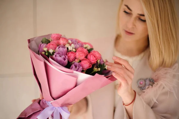 Menina no casaco olhando para o buquê de roxo flores violetas e rosa — Fotografia de Stock