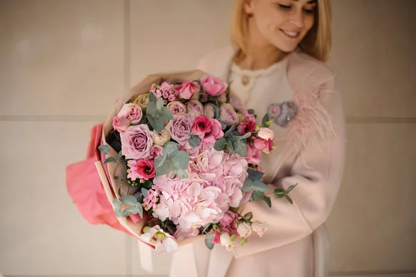 Mulher no casaco segurando um buquê de flores rosa e brancas tenras com vegetação — Fotografia de Stock