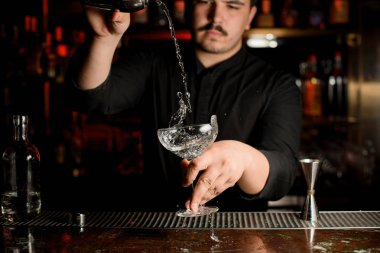 Erkek barmen çelik shaker gelen kokteyl cam içine şeffaf bir alkol döküyor