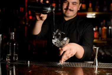 Gülümseyen erkek barmen çelik shaker gelen kokteyl cam içine şeffaf bir alkol döküyor