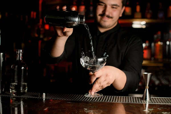 Barman sorrindo derramando um álcool transparente no copo de coquetel da coqueteleira de aço — Fotografia de Stock