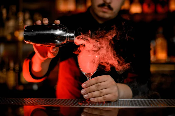Professionelle männliche Barkeeper gießt einen Rauch in das Cocktailglas aus dem Shaker — Stockfoto