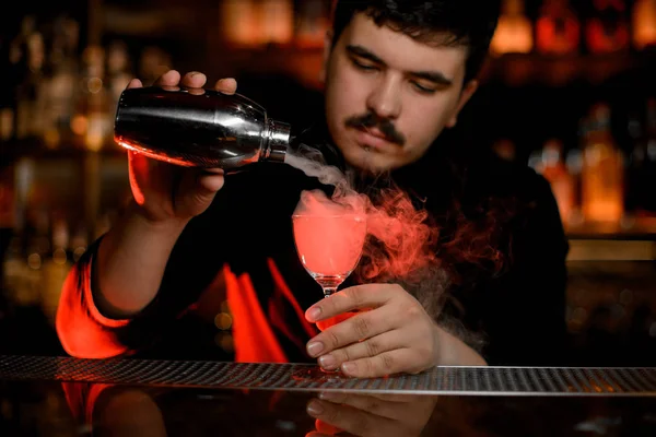 Профессиональный бармен с усами, наливающий дым в коктейльный бокал из шейкера — стоковое фото