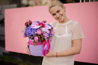 Gülümseyen kız yay ile şapka kutusunda buket tutar