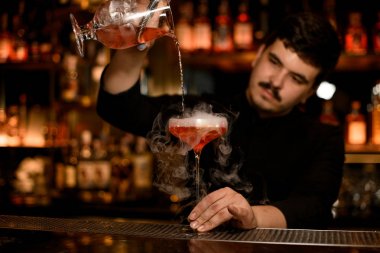 Barmen bir alkol içecek hazırlamak için süzgeç kullanır