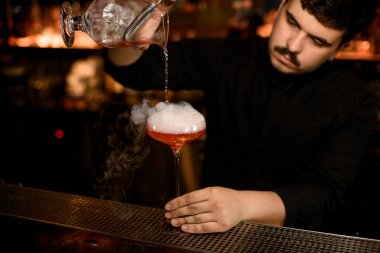 Barmen bir alkol içeceği dökmek için süzgeç kullanır