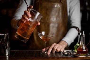 Profesyonel erkek barmen kokteyl bardağına ölçüm fincan lezzetli bir kahverengi alkollü içecek dökme