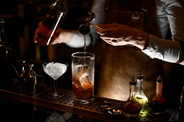 Мужчина-бармен наливает спирт из стального стального стакана в мерный стеклянный стакан — стоковое фото
