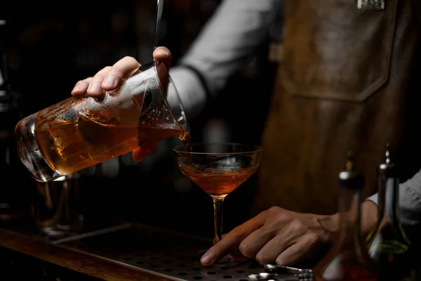Профессиональный бармен наливает коричневый алкогольный напиток из мерного стакана в коктейльный стакан — стоковое фото