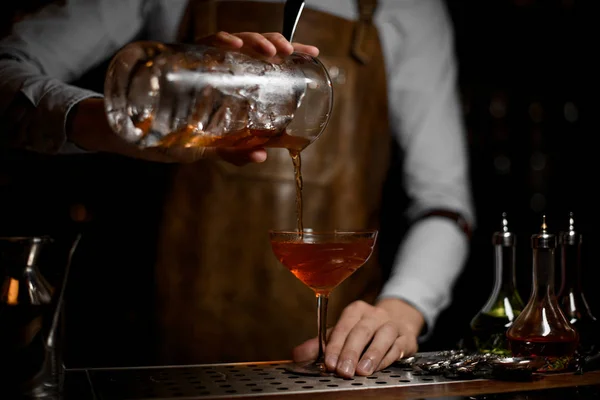 Barista versare una bevanda alcolica marrone dal misurino al bicchiere da cocktail — Foto Stock