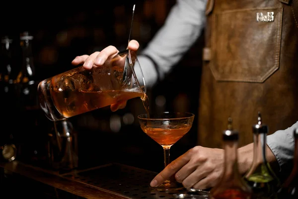 Barman masculino derramando uma bebida alcoólica marrom do copo de medição para o copo de coquetel — Fotografia de Stock