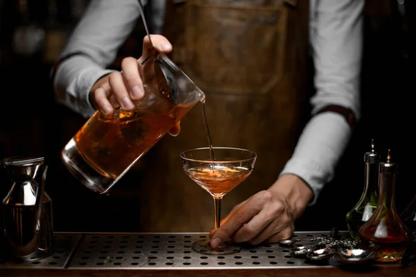 Barman professionnel masculin versant un cocktail alcoolisé brun de la tasse à mesurer au verre — Photo