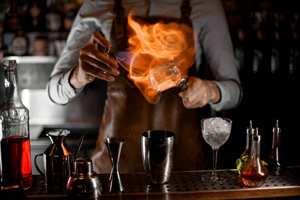 Barman colocando um fogo no cubo de gelo grande em pinças acima da coqueteleira de aço — Fotografia de Stock