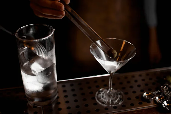 Cantinero masculino profesional poniendo una aceituna con pinzas al vaso de martini — Foto de Stock