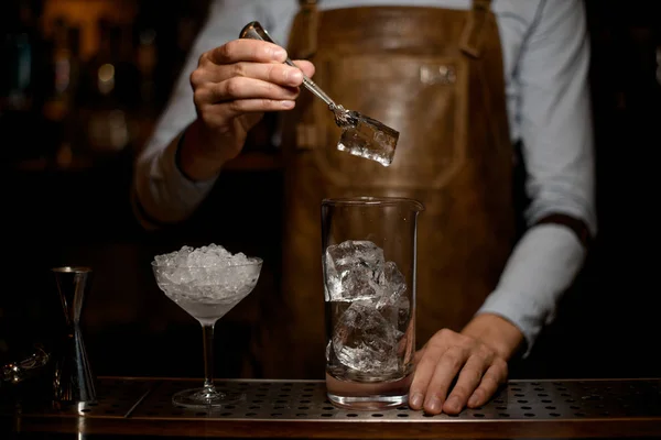 Чоловік бармен кладе великий кубик льоду до мірної скляної чашки — стокове фото