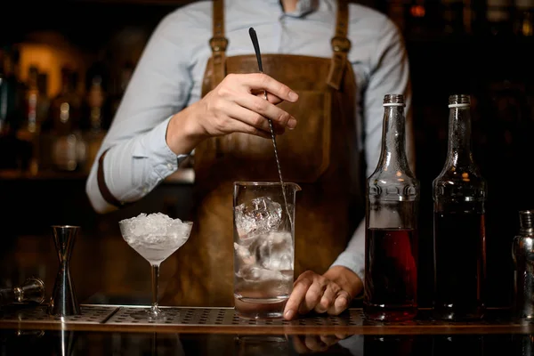 Manlig bartender omrörning en alkoholhaltig dryck med is i mätglas kopp — Stockfoto