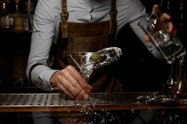 Barman macho misturando uma bebida alcoólica no copo de martini com uma azeitona — Fotografia de Stock