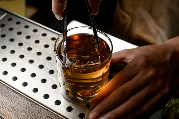 Cantinero poniendo un gran cubo de hielo al cóctel de oro en el vaso —  Fotos de Stock