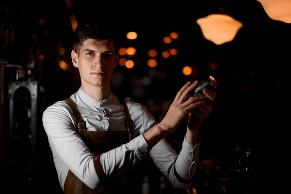Barman atraente segurando nas mãos uma coqueteleira de aço no escuro — Fotografia de Stock