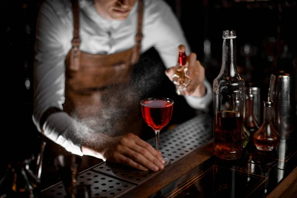 Professzionális férfi kocsmáros permetezés a piros alkoholos koktél a sötétben — Stock Fotó